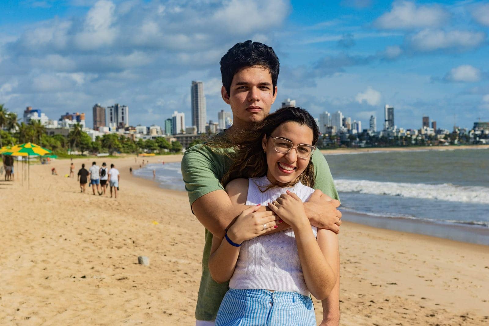 O casal abraçado olhando para a câmera na praia